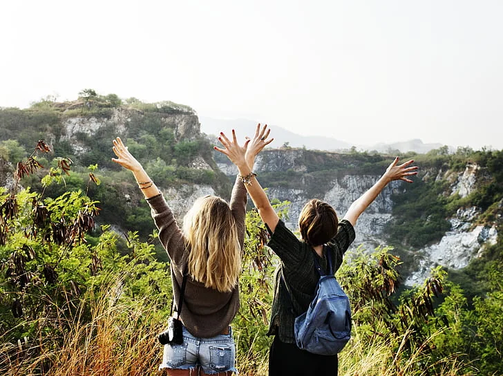Two travelers with their arms raised on a cliff overlook